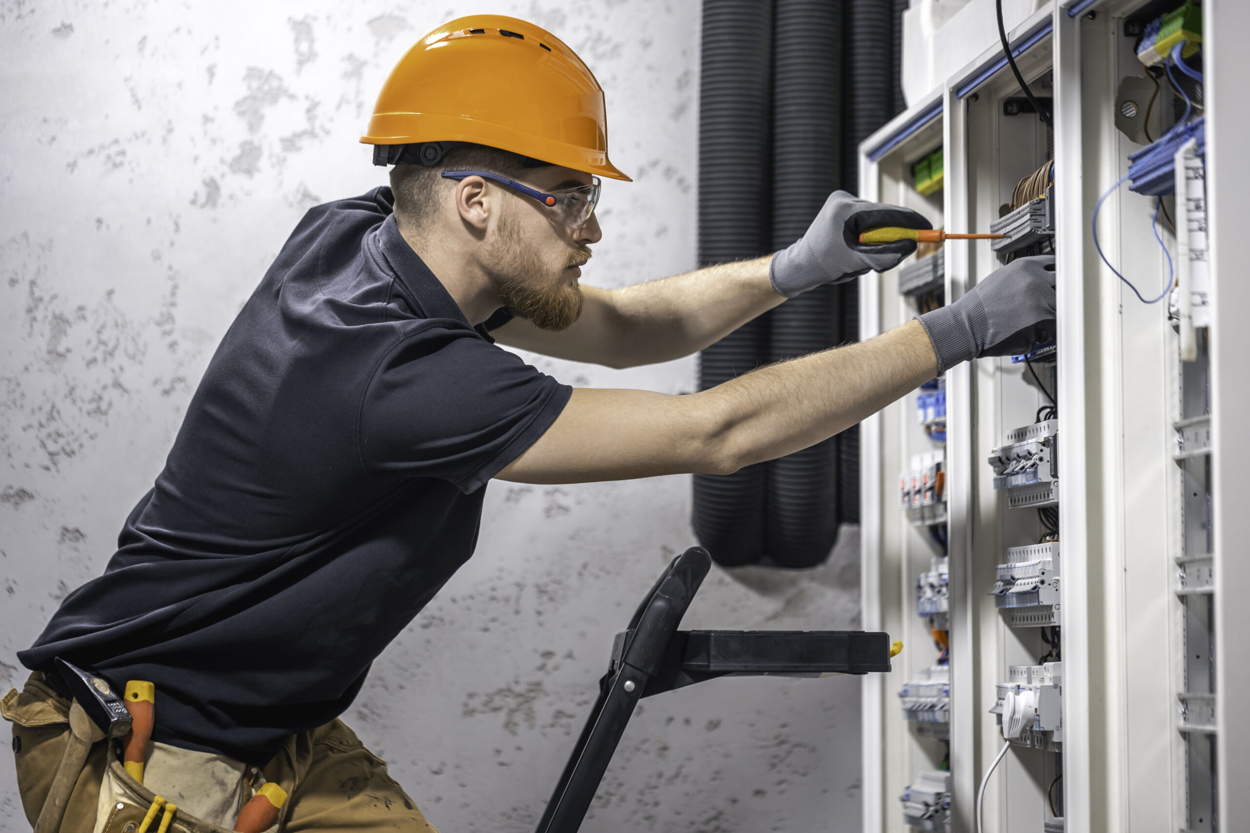 a male electrician works in a switchboard with an electrical connecting cable.